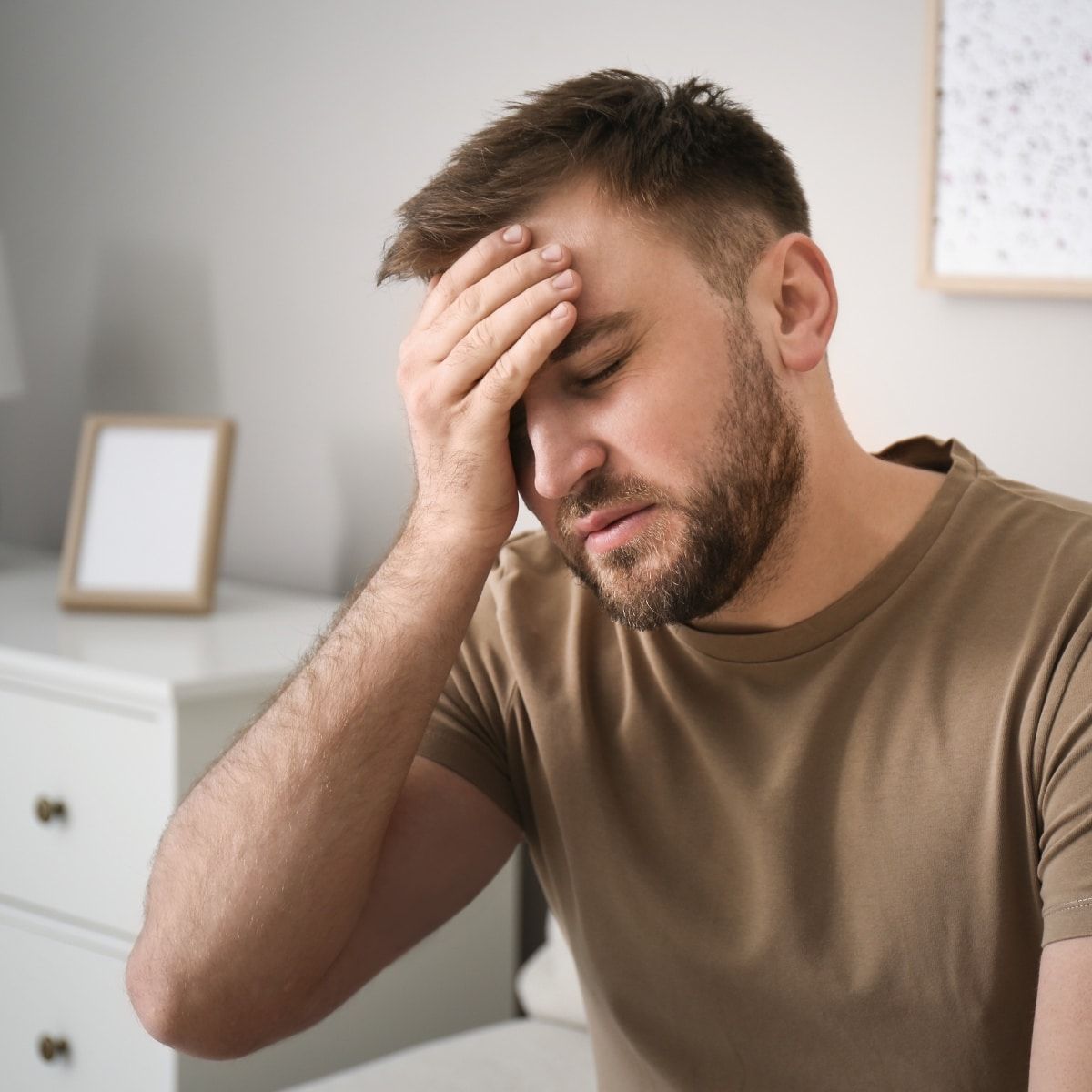 Junger Mann mit erschöpftem Gesichtsausdruck fasst sich mit einer Hand an die Stirn. Symbolbild für hochfunktionale Depression bei extrovertierten Persönlichkeiten.