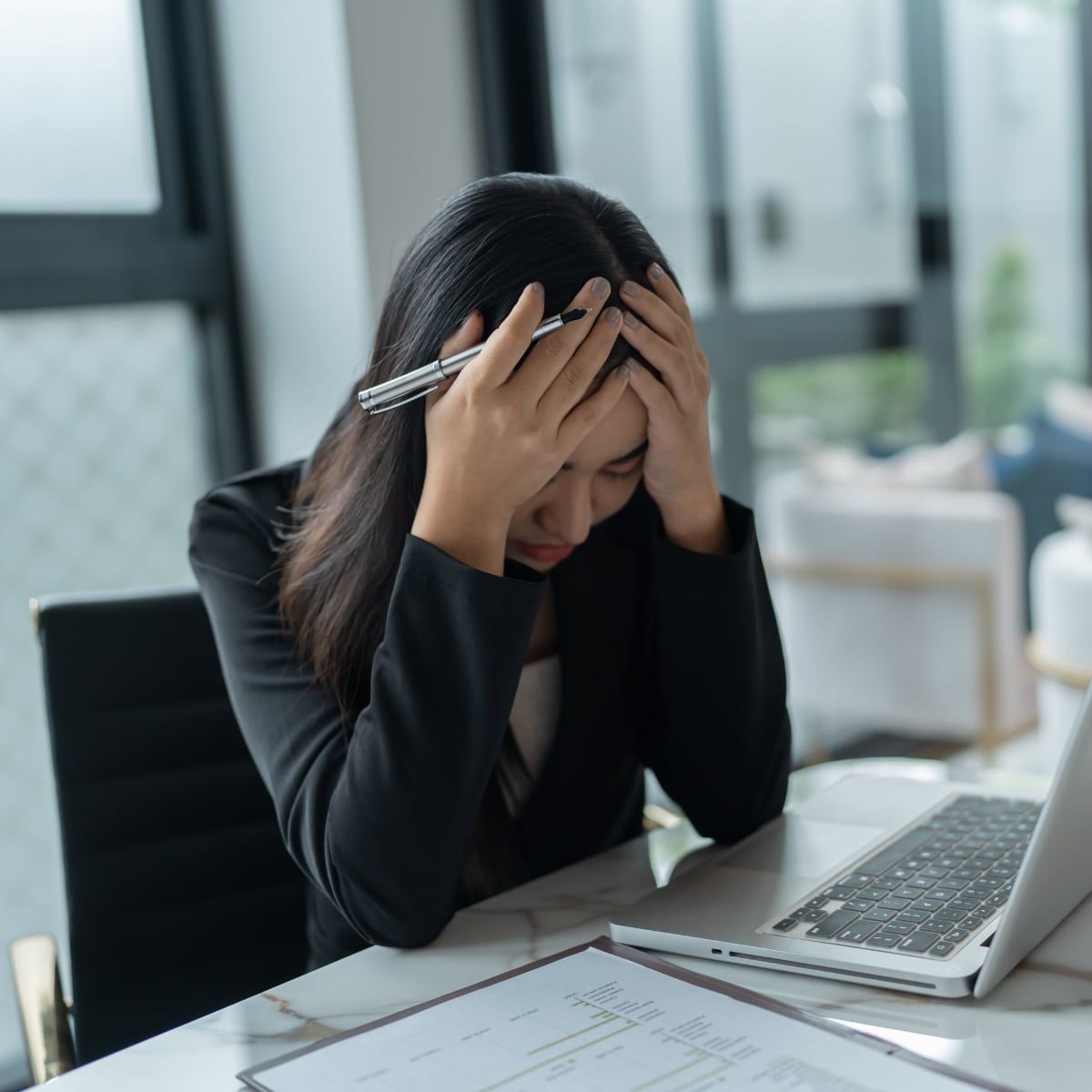 Junge, erschöpfte Frau in Arbeitsoutfit hält sich mit beiden Händen den Kopf. Symbolbild für hochfunktionale Depression im Job.