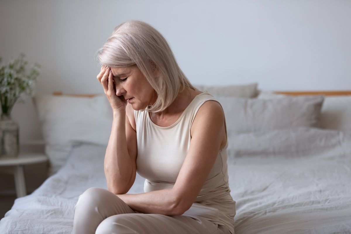 Frau mittleren Alters sitzt erschöpft und besorgt auf dem Bett – Symbolbild für Depression und seelische Belastung in den Wechseljahren.