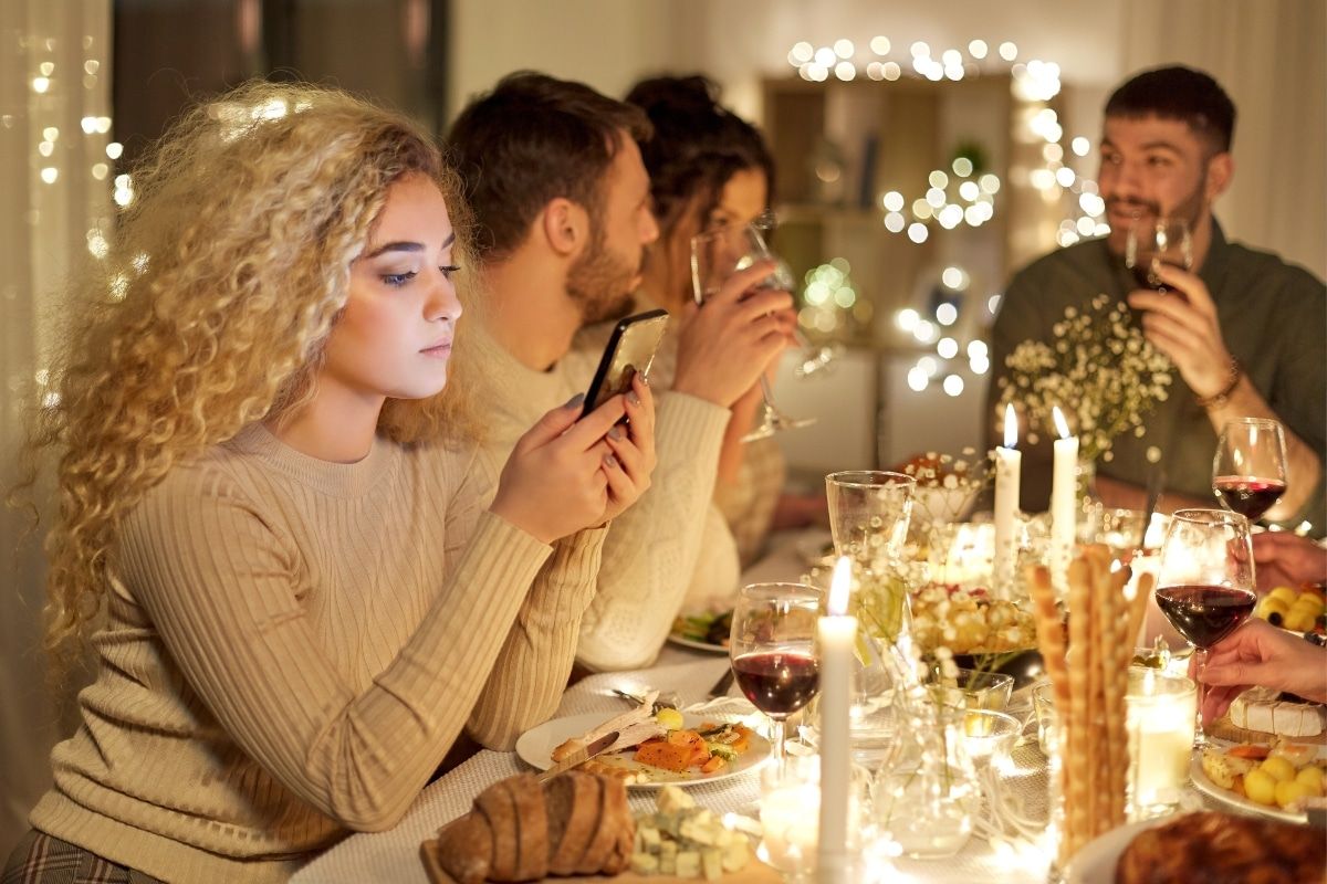 Familie beim Weihnachtessen. Eine Frau schaut nachdenklich auf Ihr Smartphone.