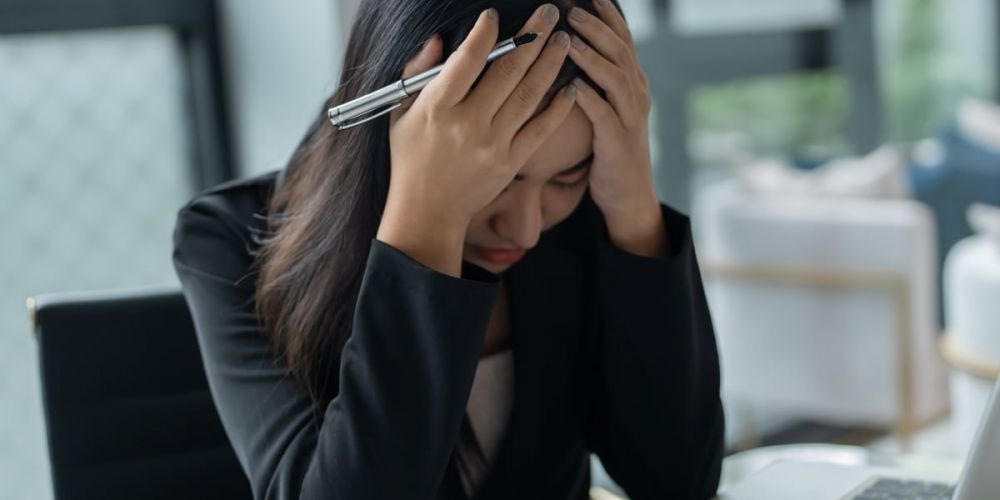 Frau in Arbeitsumgebung hält sich den Kopf – Symbolbild für Online-Selbsttest bei Stress