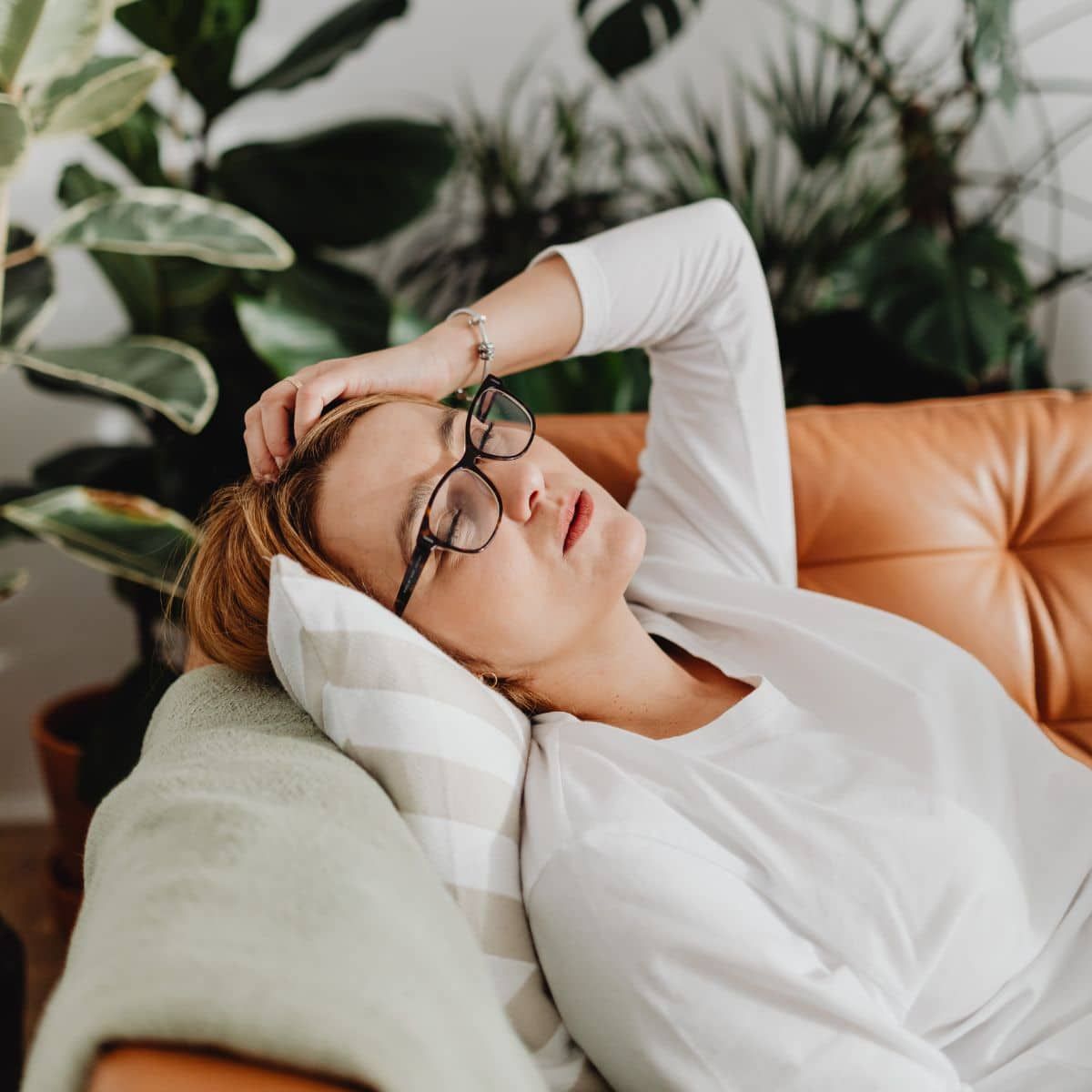 Junge Frau mit Brille liegt erschöpft auf dem Sofa und hält sich mit einer Hand den Kopf. Symbolbild für hochfunktionale Depression bei Müttern.